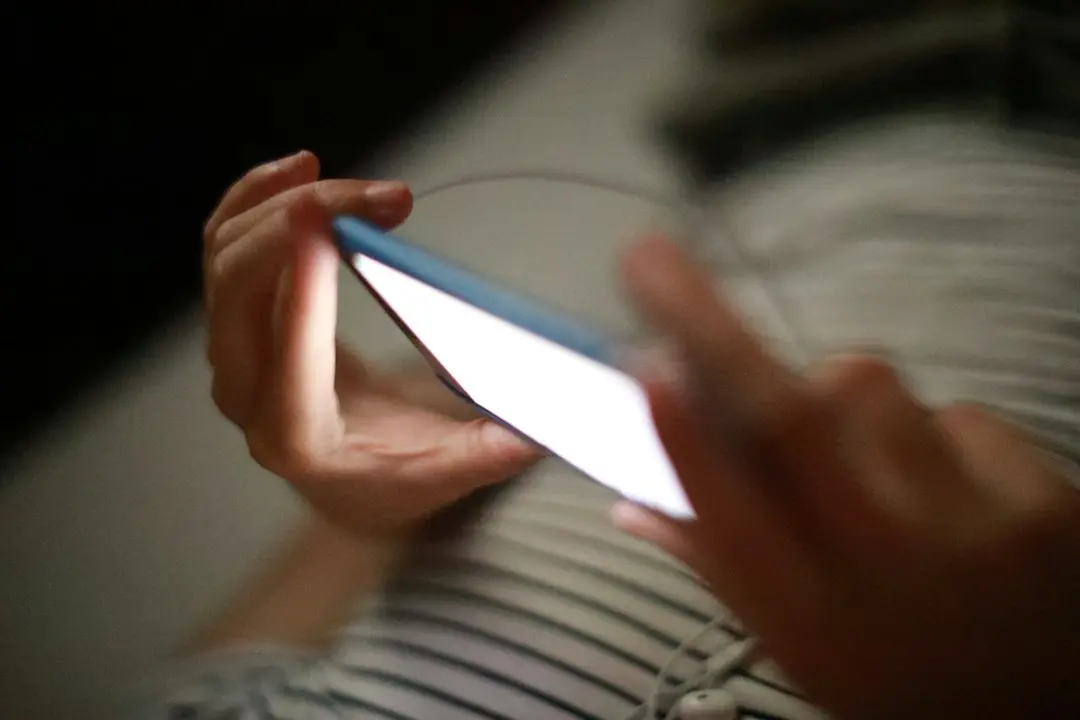 Une personne fait défiler l'écran d'un smartphone dans la pénombre, comme avec l'application Xenon IPTV